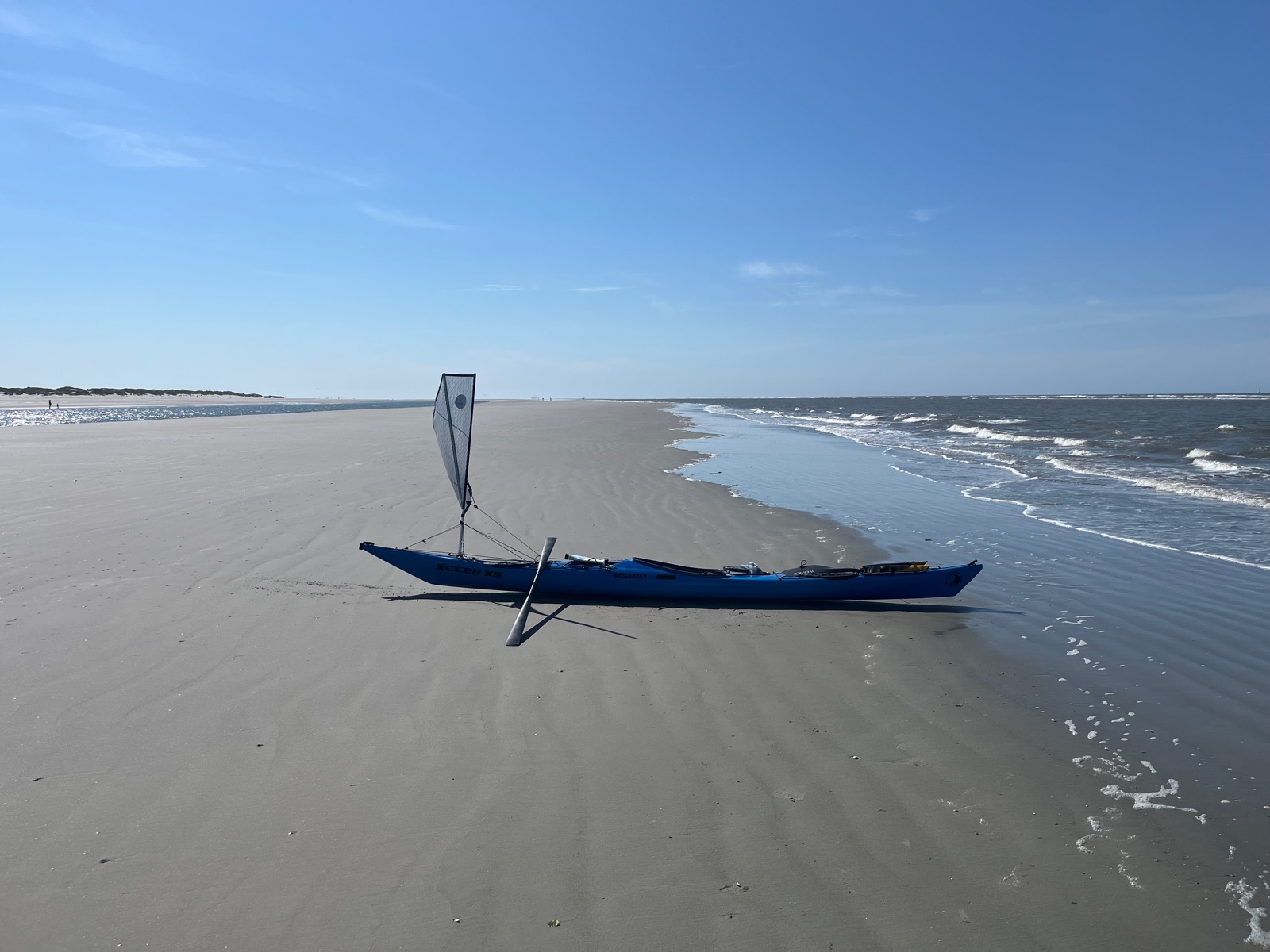 The kayak with its sail up on a wide beach by the North Sea